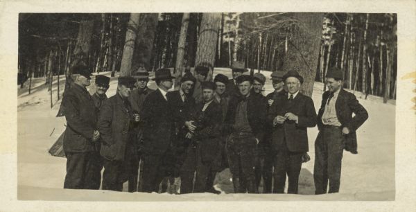 Group portrait of men standing outdoors in the snow. Trees are in the background.
