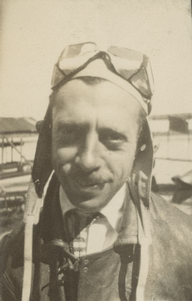 Head and shoulders portrait of Jack Vilas, air pilot, standing outdoors, wearing goggles on his head.