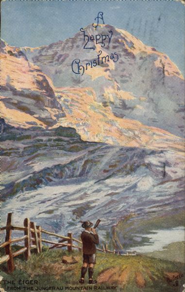Christmas postcard of a mountain peak, the Eiger, in Switzerland. In the foreground, a man is dressed in a traditional costume, blowing a horn. Text on the top reads: "A happy Christmas" and in the lower left: "The Eiger. From the Jungfrau Mountain Railway." Text on the reverse reads: "The Eiger is one of the prominent peaks in the Grindelwald district of the Bernese Oberland. It rises to a height of 13,040 feet and was first ascended by Mr. Charles Barrington in 1858. It was a difficult climb, but the prospect from such an altitude is very fine. A good view of the Eiger is obtained from the Jungfrau Mountain Railway which conducts tourists into the heart of the Jungfrau."
