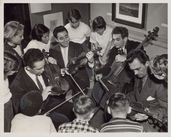 Four men are holding string instruments, while several children are looking on. Caption reads: "<b>A quartet of New York musicians</b> who played Saturday at the Milwaukee Art institute for the Junior league's children's arts program explained instruments. The men are (from left) Broadus Erle, Matthew Raimondi, Aldo Parisot, and Walter Trampler."