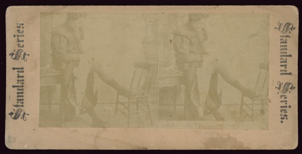 Stereographic image of a woman adjusting the garter strap to her stocking. Under right image is the caption: "I wonder why this elastic won't hold." Stereograph reads "Standard Series" on either side.