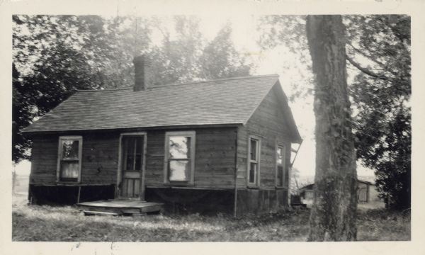 View toward a wooden house, surrounded by trees. Caption reads: "This ancient dwelling of Louise Fowler, a pioneer Brothertown Indian, is the only dwelling of a Brothertown Indian on an original allotment of land near Lake Winnebago, Wisconsin."