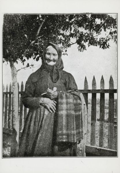 Portrait of a woman, who is wearing a dress and a kerchief knotted around her hair. She is holding some cloth over her arm, and an unidentified object in her left hand. Caption reads: "Oneida woman Copied from <u>The Oneidas</u> by J K Bloomfield (New York: James Stewart 1909) pg 264".