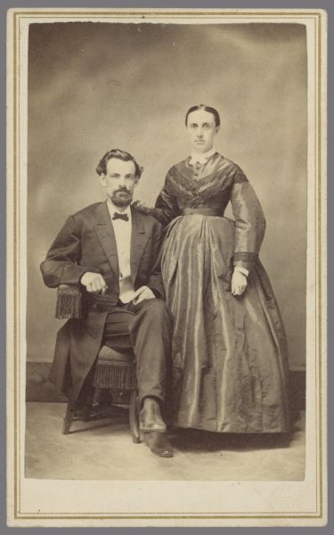 Carte-de-visite portrait of a man seated, with a woman standing next to him. Caption reads: "Rev. Jas. Gillespie & wife. Preached in Necedah over 50 years ago. [1930]. Please return: Mrs. E.L. Stillson, Necedah, Wis." Rev. Gillespie's wife was Frances Sybil Clark. Gillespie died in 1873.