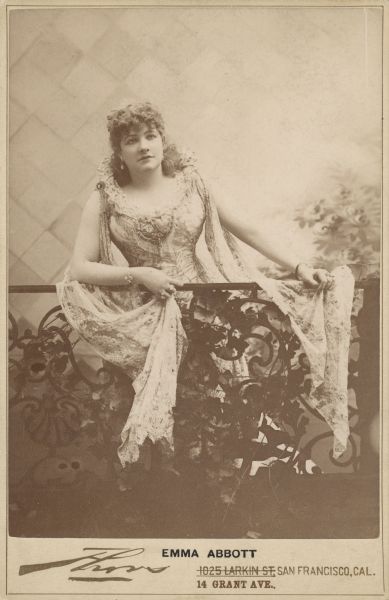 Posed portrait of opera singer Emma Abbott, leaning on a railing. Abbott was one of the most popular American opera performers of the 19th century. She was also the organizer of the Emma Abbott Grand English Opera Company.