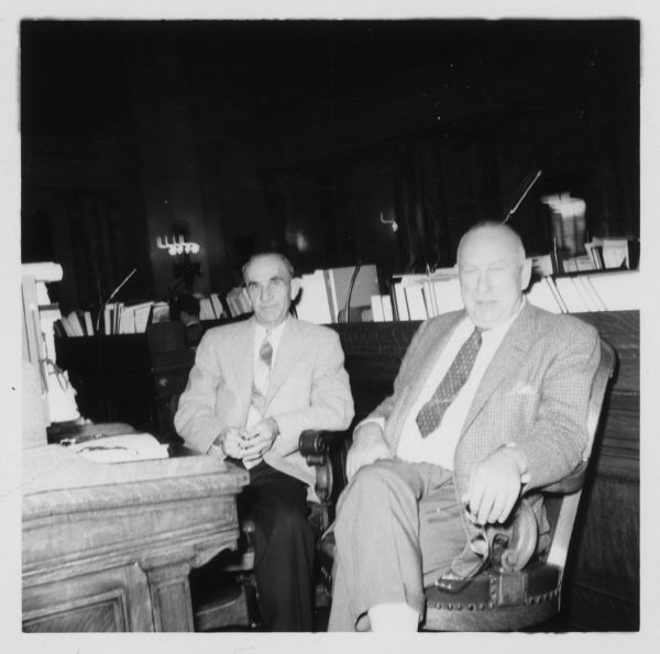 Two men are seated together. The man on the left is George J. Talsky, a Democratic member of the Wisconsin State Assembly, 1957-1960. The man on the right is Harvey Abraham, a Republican member of the Assembly, 1947-1960. Both men served on the Committee on Excise and Fees.