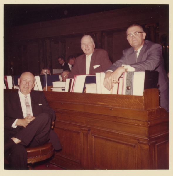Three men pose together around a wood desk. They are identified as (from left): Harvey Abraham, Gil Hipke, and [Everett] Cy Bidwell. All three were Republican members of the State Assembly in the late 1950s. Abraham and Hipke were also both World War I veterans.