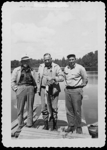 Group portrait of Republican State Assembly members Bob Matheson and Harvey Abraham (with a third, unidentified person) standing on a dock. Abraham is holding a muskellunge. Caption reads: "Bob Matheson, Harvey Abraham & Muskie (A Keeper)."