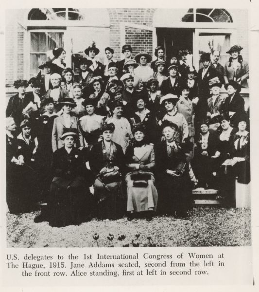 Group portrait of a group of women sitting and standing outside a building. Caption reads: "U.S. delegates to the 1st International Congress of Women at The Hague, 1915. Jane Addams seated, second from the left in the front row. Alice [Hamilton] standing, first at left in second row."