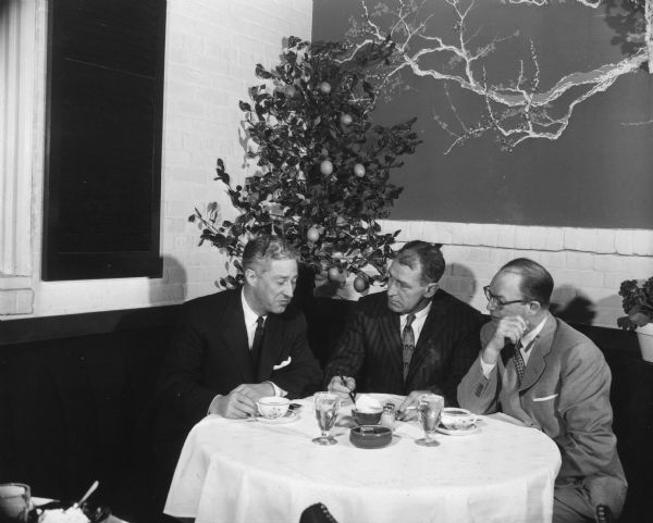 Three men sit at a table with coffee cups in front of them. A caption identifies them as "Dean [sic] Adams and friends." Deane Adams was co-founder of the Simon House Restaurant.