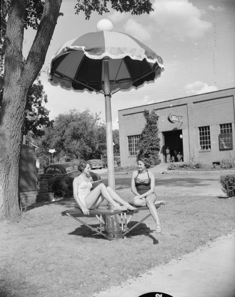 Caption reads: "Cambridge, Wis. Girls posing on seat built around lampost [sic] that has sun umbrella over it."