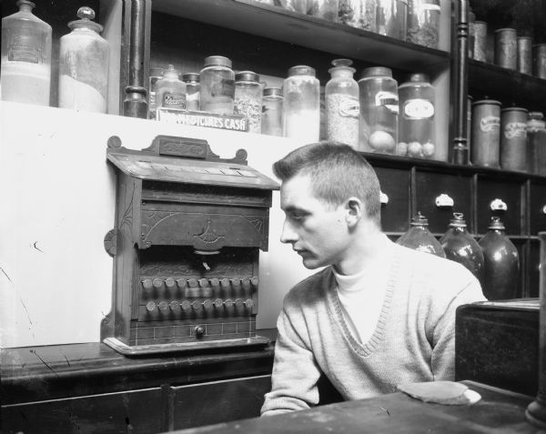 Caption reads: "Rodney Coenen, museum exhibit preparator, in the early drug store exhibit in the museum of the State Historical Society."