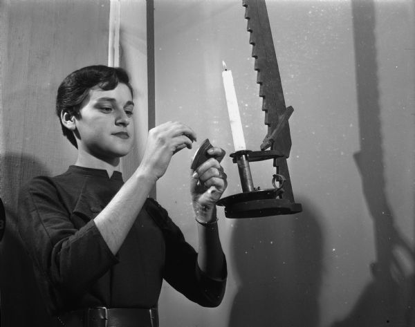 Caption reads: "Bernadette Bowers, museum office secretary, lighting candle in a candle jack displayed in the museum of the State Historical Society."