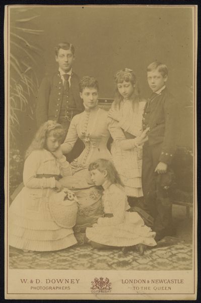 Carte-de-visite group portrait of Alexandra of Denmark, Queen consort of the United Kingdom and the British Dominions, and Empress consort of India, 1901-1910. She was married to King-Emperor Edward VII. She is seated and surrounded by her children: Prince Albert Victor, Duke of Clarence and Avondale, George V of the United Kingdom, Louise, Princess Royal, Princess Victoria, and Princess Maud of Wales.