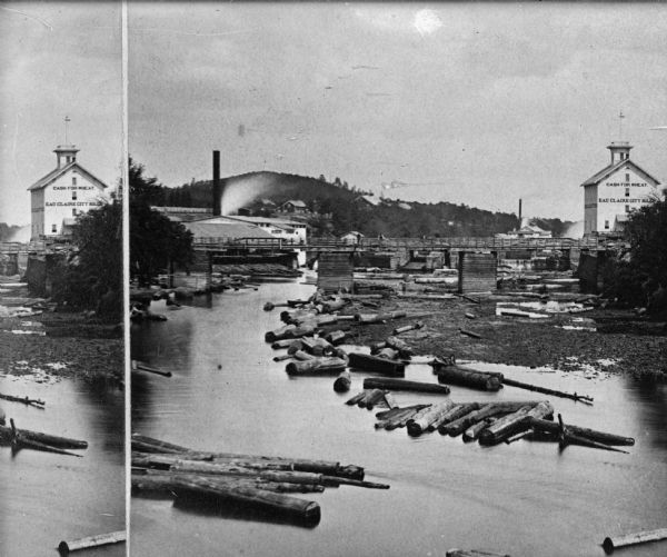 View of a lumber mill and logs floating on a river, which is spanned by a bridge. The mill has a sign that reads: "Cash for Wheat - Eau Claire City Mill." Caption reads: "Eau Claire Lumber Company and the Upper Eau Claire Bridge about 1880."