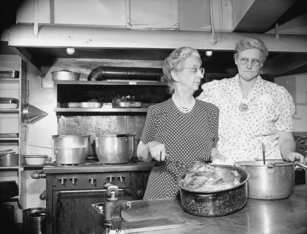 Two women pose with pots in a large kitchen. Caption reads: "madison. emily krahn retirs [sic] at yw [sic]."