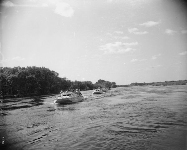 Groups of people are on four or five boats traveling on the Wisconsin River, with a shoreline behind them on the left. In the distance is the opposite shoreline. Caption reads: "Necedah, (vicinity), Wis. Petenwell Dam dedication."