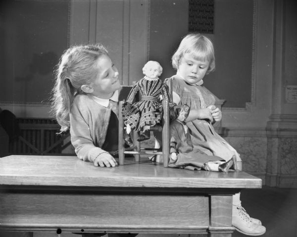 Two girls looking at dolls on a table. Caption reads: "Exhibit of children's toys. About Christmas, 1948."