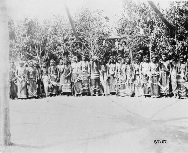 A group of men posing together in front of a stand of trees. Caption reads: "Indian 'Sun Dance' near Fort Washakie, Wyo, 1900."