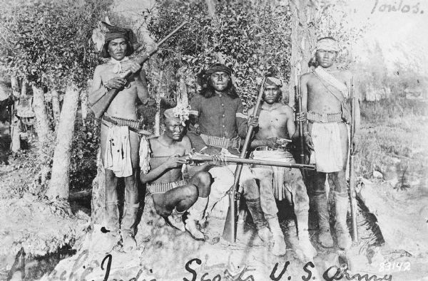 Copy photograph of several young men posing with rifles. Caption reads: "Apache Indian scouts on duty with the 6th Cavalry at Fort Wingate. New Mexico."