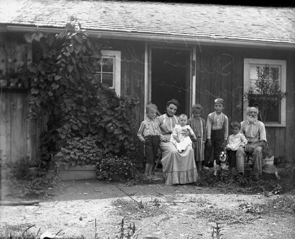 Group portrait of 7 family members and a dog posing outside a home. Caption on envelope reads: "Family of Swiss Cheese makers. 1905."