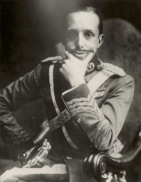Portrait of Alfonso XIII, King of Spain, who is seated and holding his chin in his hand. Caption reads: "Photograph by Western Newspaper Union. Latest photo of King of Spain. This is the most recent photograph taken of King Alphonso of Spain whose country is having all sorts of internal trouble."