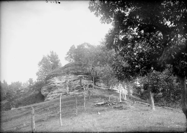 View looking up a grassy hill along a fence towards a rock formation. Four people, a man with three children, are posing at the base.