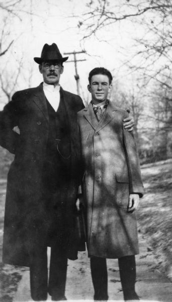 UW-Madison sociology professor Edward Alsworth Ross posing with his arm around his son Gilbert. They are standing outdoors; both men are wearing coats, and Edward is wearing a hat.