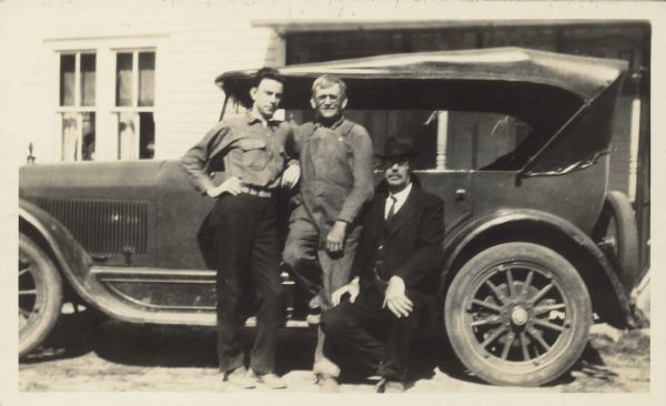 Three men pose along a car. Caption reads: "Edward Alsworth Ross, with son Gilbert Ross, and local farmer, on fishing trip, Otsego, Wis. Probably early 1920's."