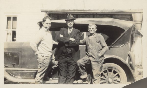Three men pose along the side of a car. Caption reads: "Edward Alsworth Ross, with son Frank A. Ross and local farmer, on fishing trip, Otsego, Wis. Early 20's."