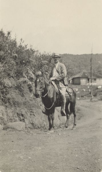 UW-Madison sociology professor Edward Alsworth Ross poses on horseback on an unpaved road. A building is in the distance. Caption reads: "This is for Mrs. Ross with my compliments. H.R.P. Caracas, 24-10-13."