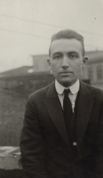 Portrait of Arthur J. Altmeyer, who would be a key figure in developing the U.S. Social Security system, as a young men. Appears to be around the time he was a graduate student at UW-Madison under John R. Commons. A building is visible behind him.