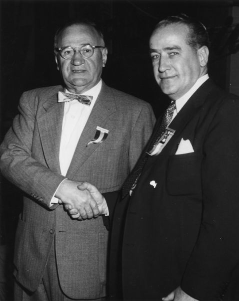 Textile Workers Union of America [TWUA] General President Emil Rieve and Executive Vice President William Pollock posing shaking hands. A caption identifies the setting as the 1954 TWUA convention.