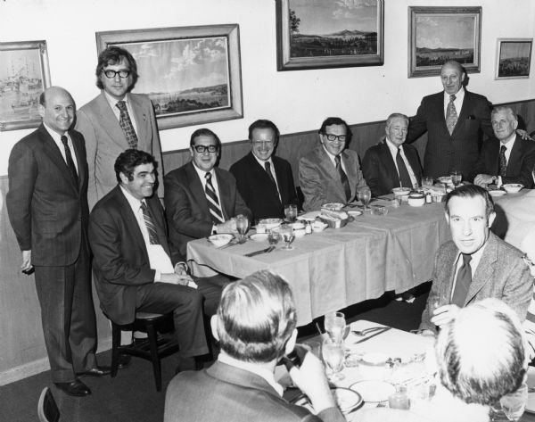 Twelve men are seated or standing in a dining room. Caption reads: "Mtg with Heinz Ruhnau, Senator for Internal Affairs of Hamburg."