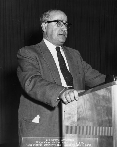 A man stands at a podium. He is TWUA General President William Pollock. Caption reads: "1st Annual Convention. North Carolina State A.F.L.-C.I.O. Park Center, Charlotte, N.C. March 19,20,21, 1958."
