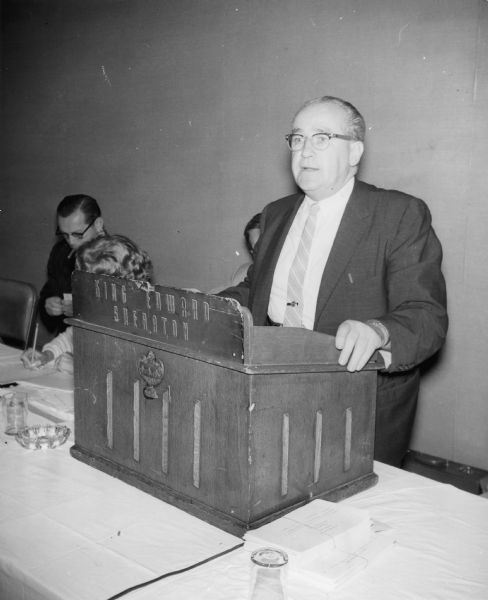 A man stands at a podium for the King Edward Sheraton hotel. Other people are behind him. Caption reads: "Main speaker at the recent Canadian Defense Fund Conference in Toronto was General President William Pollock."