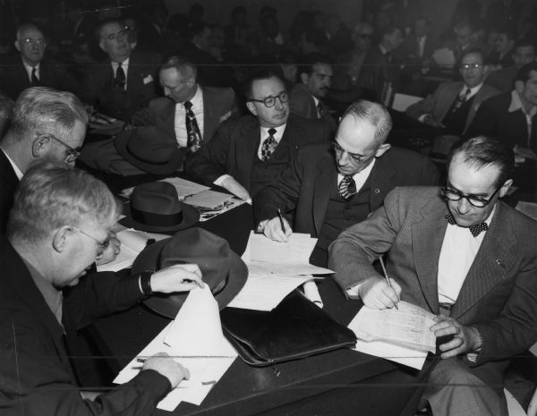 Several men are seated at a table, some of them filling out forms. Others people are in the background. Caption reads: "U.S. delegates registering at ICFTU [International Confederation of Free Trade Unions] Western Hemisphere conference, Mexico City. Jan. 1951. L to R: Fred Dowling of the CIO Packinghouse Workers, fr. Canada; Martin Kyne, of the CIO Wholesale and Retail Clerks; Dr. Ernst Schwarz, secy.; CIO Latin Am. Committee; David McDonald, secy-treas. CIO Steel Workers; John Brophy, ICFTU rep. at U.N.; Wm. C. Doherty, pres. Letter Carriers, AFL; E. O. Knight, pres., CIO Oil Workers; Lewis Clark, secy-treas CIO Packinghouse Workers; L. S. Buckmaster, pres. CIO Rubbert [sic] Workers; and Wm. Pollock, secy-treas CIO Textile Workers."