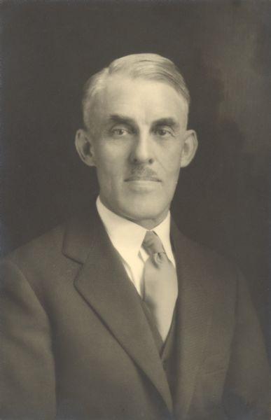 Waist-up portrait of Jesse Hazen "J.H." Ames, president of the River Falls Normal School (1917-1927), and its successor the River Falls State Teachers College (1927-1946), now the University of Wisconsin-River Falls. Ames was a student of Frederic Jackson Turner, and the co-author of four Elementary history textbooks, with his brother Merlin McMain Ames.
