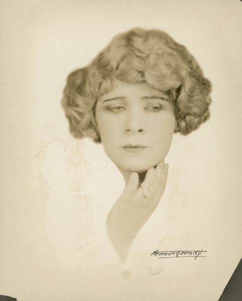 Head shot of Mae West - only her head and one of her hands is seen.  She looks pensively to the side.  Her hair is short and curly.