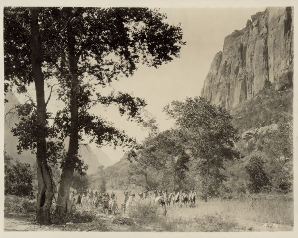 Photograph of men, dressed as Native Americans, on horseback for the 1928 film "Ramona".  The men and horses are dominated by a large tree on the left and mountains on the right and in the background.
