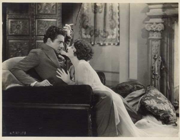 Scene from the 1926 film "Camille" starring Norma Talmadge and Gilbert Roland.  Roland sits on a couch and recoils as Talmadge, who is kneeling in front of him, pleads with him.
