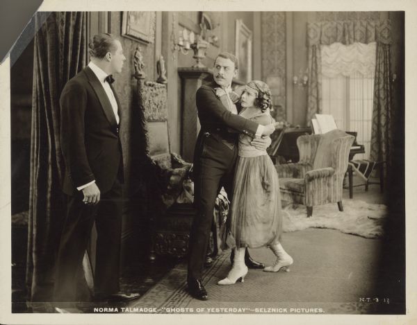In a scene from the 1918 film "The Ghosts of Yesterday", Norma Talmadge, as Jeanne La Fleur, tries to get away from Count Pascal de Fondras, played by Stuart Holmes.  Howard Marston, played by Eugene O'Brien, stands in the doorway and looks at the two.