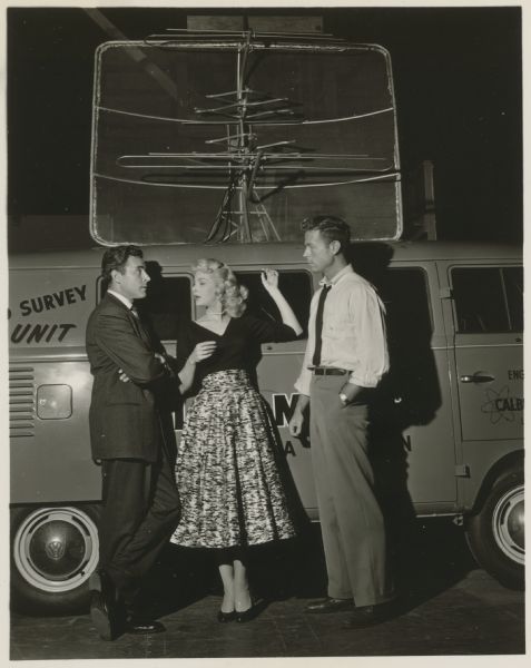 Peter Hansen, Jan Shepard, and Charles Maxwell stand in front of a truck with a large antenna on its roof in a scene from the Ziv-TV show Science Fiction Theatre.  The scene is from the episode entitled "The Strange Lodger".