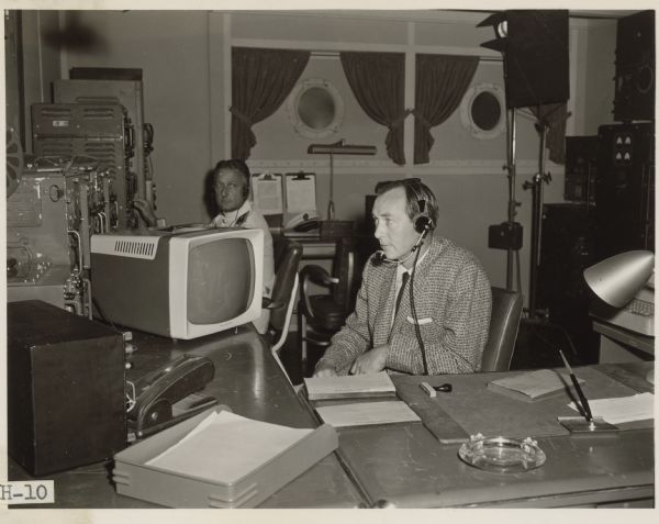 Actor Robert Shield, playing Dr. Robert Werth, sits at a desk in a scene from the episode Signals from the moon of the Ziv-TV show Science Fiction Theatre.  He wears a headset with a microphone.  A man sits in the background and operates equipment.