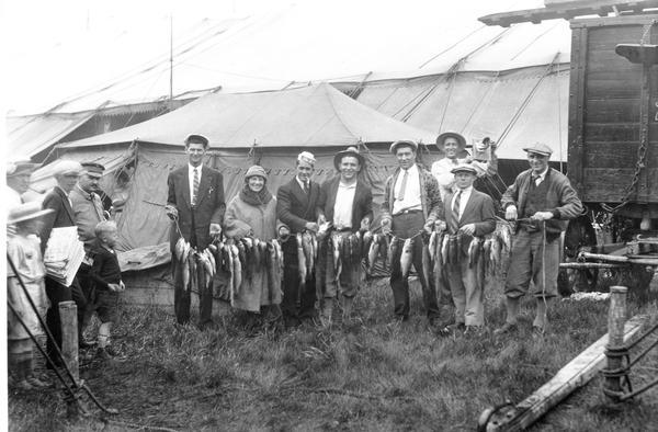 A crew of people from the circus, possibly Ringling Brothers, Barnum, and Bailey, holding up their catch after a fishing trip.