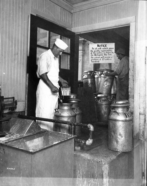 Dairyman conducting Methylene blue test on a can of milk. Notice in background reads: "For all milk which passes the quality requirements of this factory, as shown by the Methylene Blue Test, the patron will receive a premium of 25 cents a hundred."
