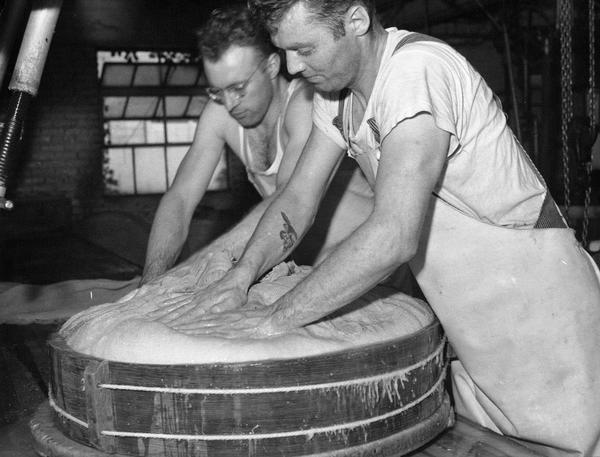 Two men pressing the curd into a form at the Swiss Cheese Factory.