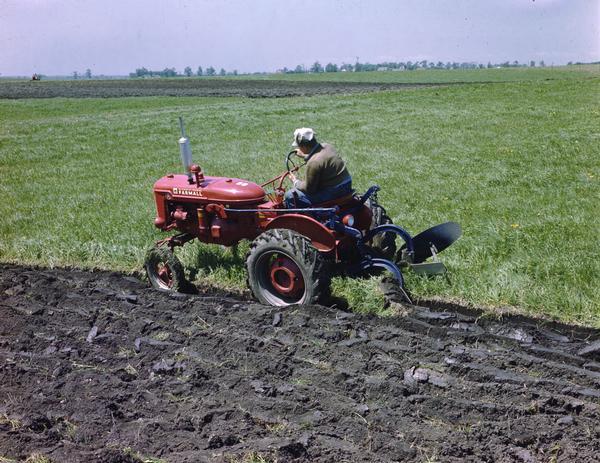 A man driving a Farmall Super A tractor in a field.