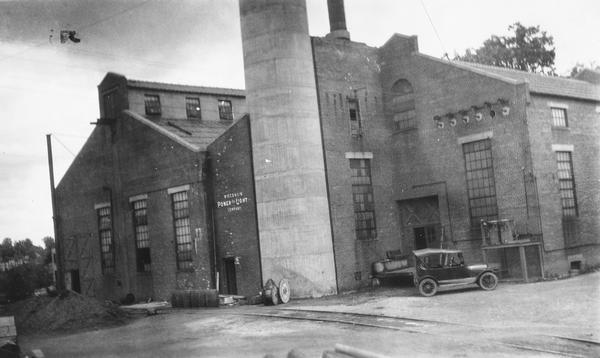 Exterior shot of a vacant factory building with a car parked in front taken as part of a survey by the Wisconsin Power and Light Company to promote economic development by emphasizing available buildings and building sites.