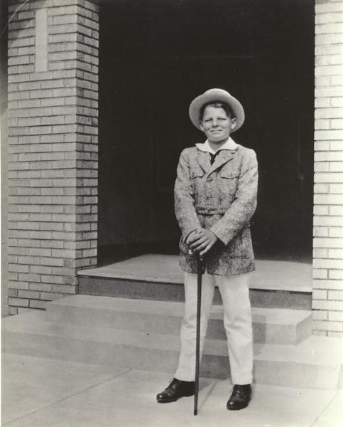 Jack Carson at the age of ten posing on front steps wearing a hat and leaning on a walking cane.